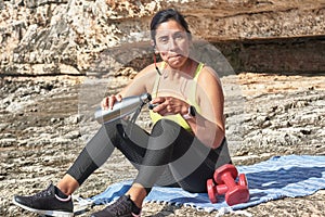 Latin woman, middle-aged, resting, regaining strength, eating, drinking water, after a gym session, burning calories, keeping fit