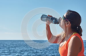 Latin woman, middle-aged, resting, regaining strength, eating, drinking water, after a gym session, wearing orange top, burning