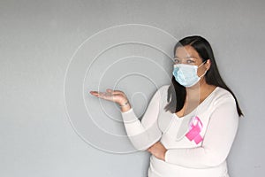 Latin woman with protection mask, black hair and white sweater with pink ribbon for campaign against breast cancer