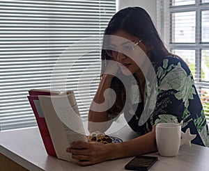 Latin woman reading a book in pajamas in the kitchen