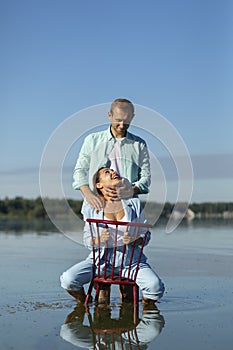 Latin woman sitting in chair in water, looking at Caucasian man, male holds, admires