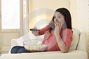 Latin woman sitting at home sofa couch in living room watching television scary horror movie