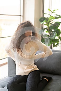 Latin woman sitting on sofa with backache feeling