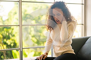 Latin woman sitting on sofa with neckache feeling