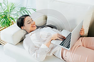 Latin woman using laptop while lying on sofa at home