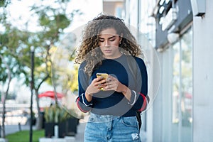 Latin woman using a mobile phone while walking outdoors on the street.