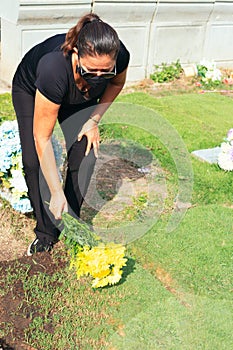 Latin woman visiting a loved one at the cemetery paying respects with fresh yellow flowers. Female grieving at graveyard