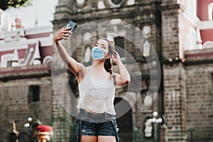 Latin Woman wearing face mask to prevent infection or respiratory illness and taking selfie photo with smartphone. Mexican girl wi