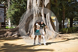 Latin women couple, young, dancing bachata with a big tree in the background in an outdoor park, performing different dance