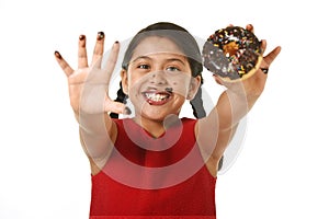 Latin young girl in red dress holding chocolate donut with hands and mouth stained and dirty showing smiling happy