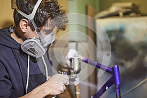 Latin young man concentrated spray painting a bicycle frame in his workshop