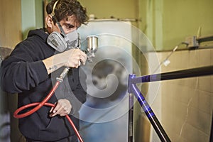 Latin young man concentrated spray painting a bicycle frame in his workshop