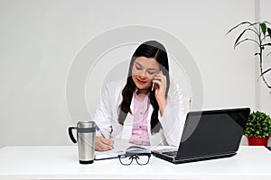 Latina doctor woman works in her office very busy uses her cell phone to answer messages, calls and video calls from patients