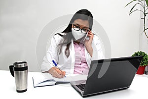 Latina doctor woman works in her office very busy uses her cell phone to answer messages, calls and video calls from patients