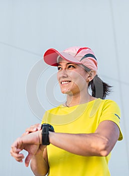 Latina female runner looking at her watch. Synchronizing her watch to go for a run. Yellow clothes and cap. Running in the street