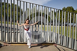 Latina and Hispanic girl, young and pretty, wearing a T-shirt made with a handkerchief and white pants, holding on to a fence with