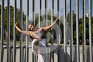 Latina and Hispanic girl, young and pretty, wearing a T-shirt made with a handkerchief and white pants, holding on to a fence with