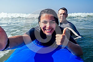 Latina-merican beautiful girl surfer instructor making selfie photo wirh friend thumbs up on camera smartphone in summer