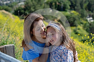 Latina Mother and Daughter Smiling and laughing on a hill in front of yellow flowers