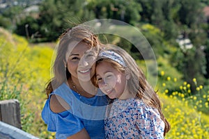 Latina Mother and Daughter Smiling and laughing on a hill in front of yellow flowers