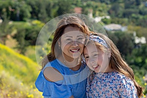 Latina Mother and Daughter Smiling and laughing on a hill in front of yellow flowers