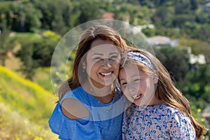 Latina Mother and Daughter Smiling and laughing on a hill in front of yellow flowers