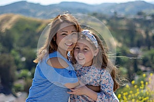 Latina Mother and Daughter Smiling and laughing on a hill in front of yellow flowers