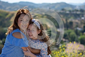 Latina Mother and Daughter Smiling and laughing on a hill in front of yellow flowers