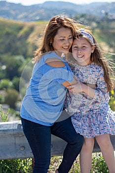 Latina Mother and Daughter Smiling and laughing on a hill in front of yellow flowers