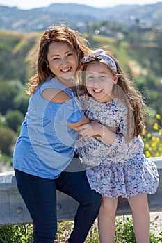 Latina Mother and Daughter Smiling and laughing on a hill in front of yellow flowers