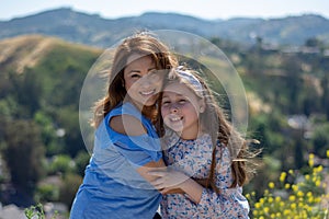 Latina Mother and Daughter Smiling and laughing on a hill in front of yellow flowers