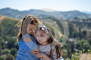 Latina Mother and Daughter Smiling and laughing on a hill in front of yellow flowers