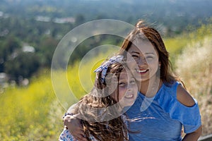 Latina Mother and Daughter Smiling and laughing on a hill in front of yellow flowers