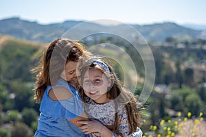 Latina Mother and Daughter Smiling and laughing on a hill in front of yellow flowers