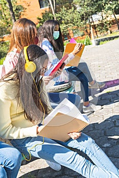 Latina teen women studying outdoors on high school campus wearing covid 19 prevention mask