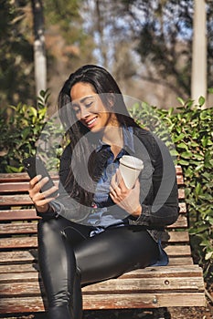 Latina woman drinking coffee and texting at the park