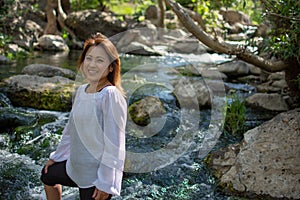 Latina woman with serious expression standing in the shade with glowing hair in a stream with waterfalls in the background
