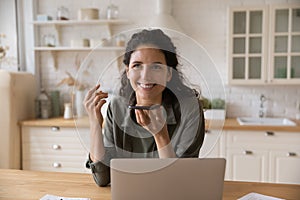 Latina woman sit at table holds smartphone talks on speakerphone