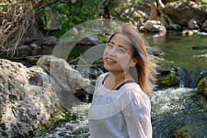 Latina woman smiling standing in the shade with glowing hair in a stream with waterfalls in the background