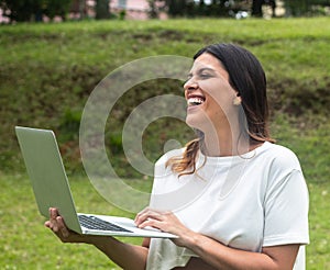 Latina woman standing with laptop in park