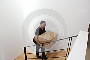 Latino adult man carries a heavy cardboard box up stairs which causes severe pain in his lower back and back