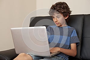 Latino boy sitting on sofa with laptop computer