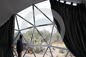 Latino man inside a geodesic glamping tent with beds and transparent roof to see the sky and stars