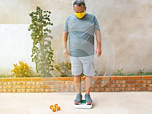 Latino man in medical mask weighs himself on a scale and is unhappy with the results