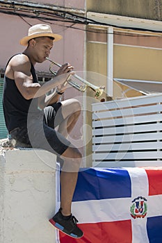 Latino man playing a trumpet sitting on a wall with the Dominican Republic flag: Selective focus.