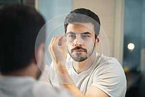 Latino man trimming eyebrow for body care in bathroom