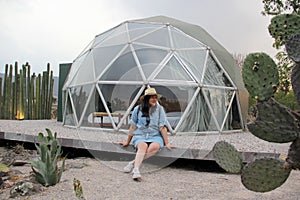 Latino woman outside a geodesic glamping tent with a roof and transparent windows to view the sky and stars