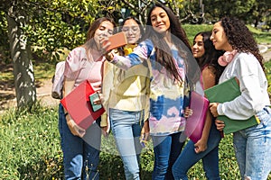 Latinx teenage friends taking a selfie with their cell phones in a park, students with notebooks and backpacks photo