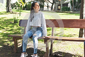 Latinx teenage girl with curly hair smiling optimistically on a park bench on a sunny day photo