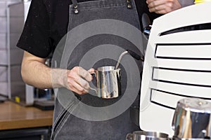 barista whips milk in a pitcher with a steam of a coffee machine photo